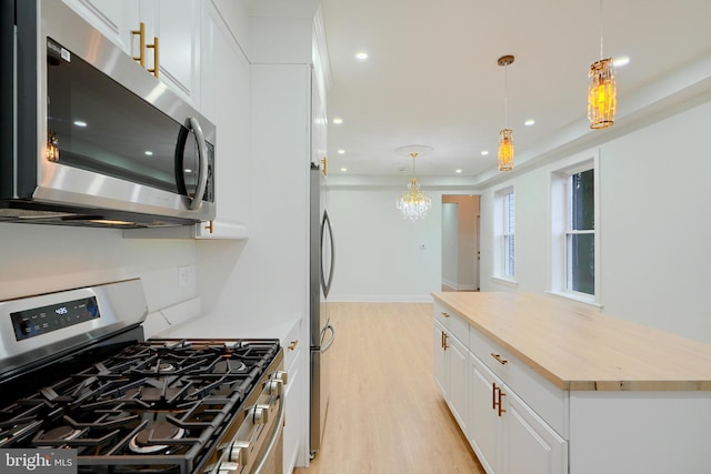 kitchen featuring stainless steel appliances, light hardwood / wood-style flooring, hanging light fixtures, and white cabinetry