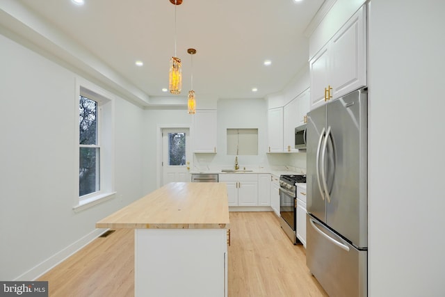 kitchen featuring wood counters, stainless steel appliances, decorative light fixtures, white cabinetry, and a kitchen island