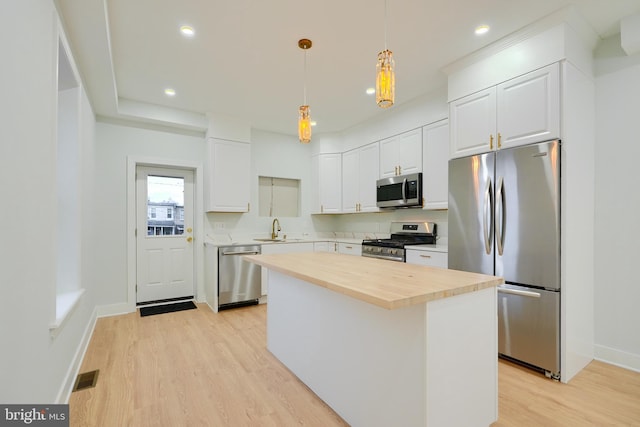 kitchen featuring decorative light fixtures, a kitchen island, white cabinetry, and stainless steel appliances