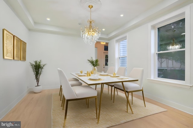 dining room featuring a notable chandelier, light wood-type flooring, and a tray ceiling