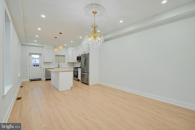 kitchen with a center island, stainless steel appliances, hanging light fixtures, light hardwood / wood-style floors, and white cabinets