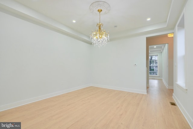 spare room with a notable chandelier and light wood-type flooring