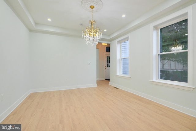 empty room with a raised ceiling, a chandelier, and light hardwood / wood-style floors