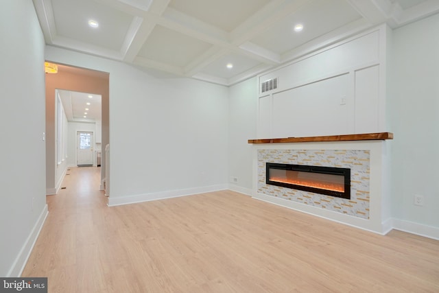 unfurnished living room featuring beam ceiling, a stone fireplace, light hardwood / wood-style flooring, and coffered ceiling