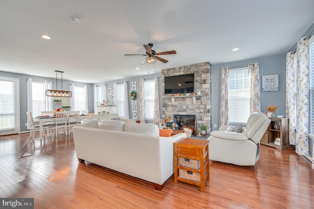 living room featuring ceiling fan, a stone fireplace, and light hardwood / wood-style flooring