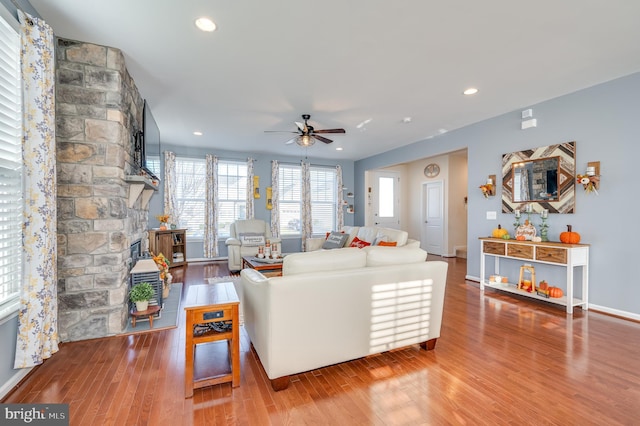 living room featuring hardwood / wood-style flooring, ceiling fan, and a stone fireplace