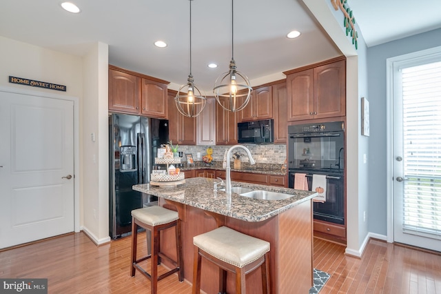 kitchen featuring sink, hanging light fixtures, an island with sink, decorative backsplash, and black appliances