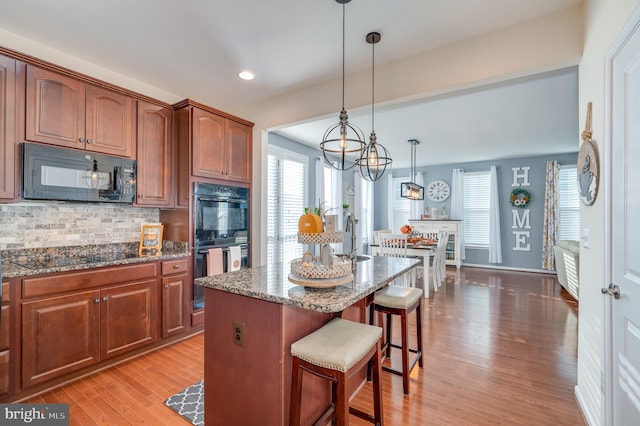 kitchen featuring tasteful backsplash, black appliances, light hardwood / wood-style flooring, hanging light fixtures, and a breakfast bar area