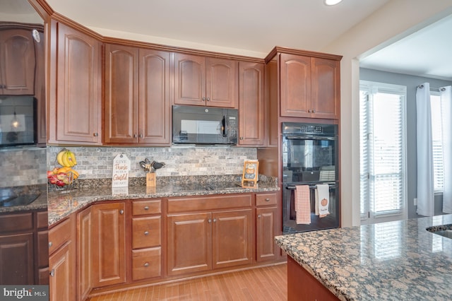 kitchen with decorative backsplash, light wood-type flooring, dark stone countertops, and black appliances