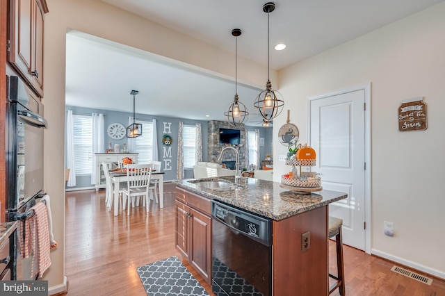 kitchen with black appliances, a center island with sink, sink, and hardwood / wood-style flooring