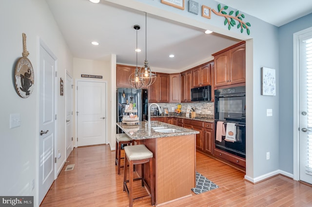 kitchen with black appliances, light hardwood / wood-style floors, a center island with sink, and light stone countertops