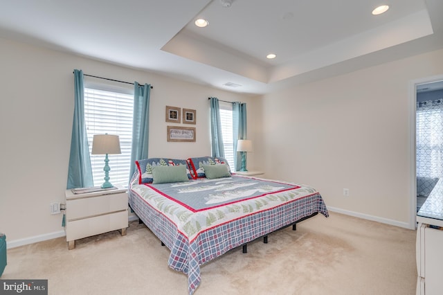 bedroom with light colored carpet, a tray ceiling, and multiple windows