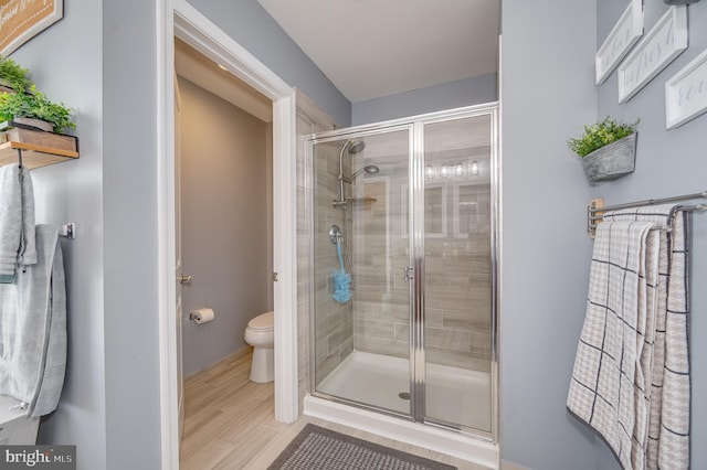 bathroom with hardwood / wood-style floors, a shower with shower door, and toilet