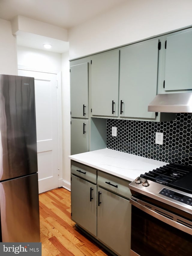 4457 Alabama Ave SE, Washington, DC 20019 - kitchen featuring appliances with stainless steel finishes, wall chimney exhaust hood, light countertops, light wood-type flooring, and backsplash