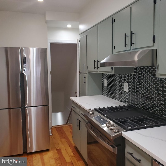 4457 Alabama Ave SE, Washington, DC 20019 - kitchen with appliances with stainless steel finishes, under cabinet range hood, light wood-style flooring, tasteful backsplash, and light stone countertops