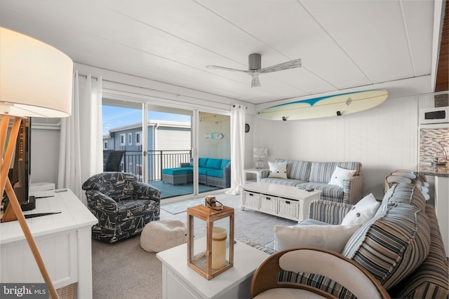 carpeted living room featuring ceiling fan and wooden walls