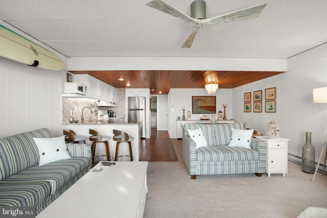 living room featuring ceiling fan, sink, light hardwood / wood-style floors, and wood walls