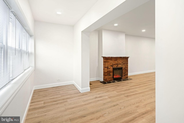 unfurnished living room with light wood-type flooring and a brick fireplace