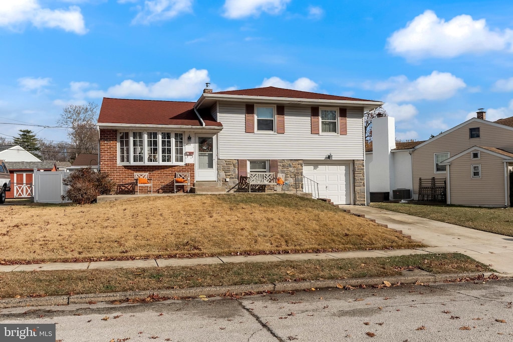 split level home featuring central air condition unit, a front yard, and a garage