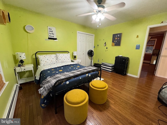 bedroom with a closet, dark hardwood / wood-style floors, baseboard heating, and ceiling fan