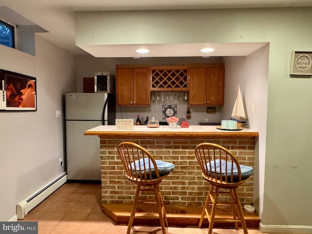 bar with stainless steel refrigerator, light tile patterned floors, and a baseboard heating unit