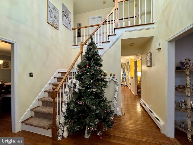 stairs with hardwood / wood-style floors, baseboard heating, and a high ceiling