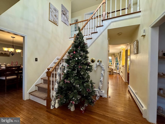 stairway with a notable chandelier, wood-type flooring, baseboard heating, and a towering ceiling