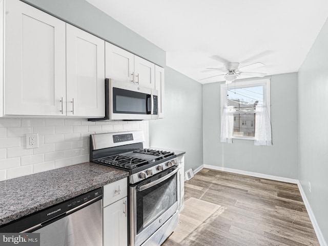 kitchen featuring backsplash, dark stone countertops, appliances with stainless steel finishes, light hardwood / wood-style floors, and white cabinetry