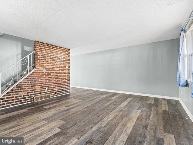 unfurnished living room featuring dark hardwood / wood-style floors, a textured ceiling, and brick wall