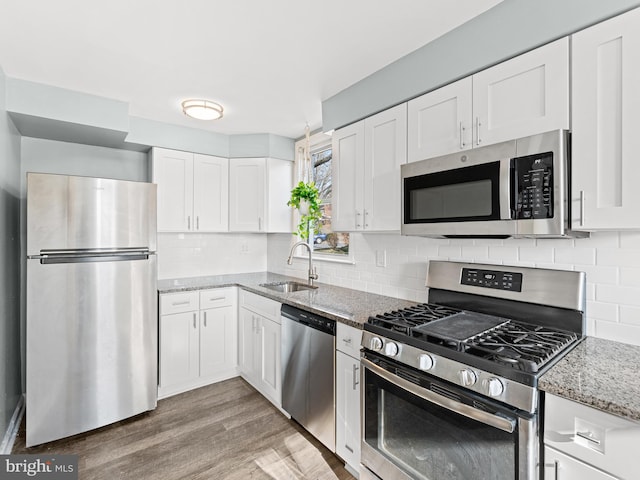 kitchen featuring white cabinets, sink, appliances with stainless steel finishes, light stone counters, and wood-type flooring