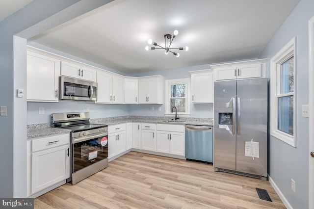 kitchen with white cabinets, appliances with stainless steel finishes, light hardwood / wood-style flooring, and light stone counters