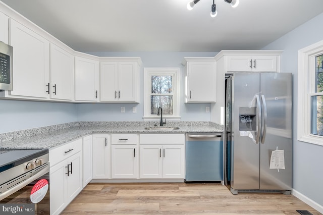 kitchen featuring white cabinetry, sink, light stone counters, appliances with stainless steel finishes, and light wood-type flooring