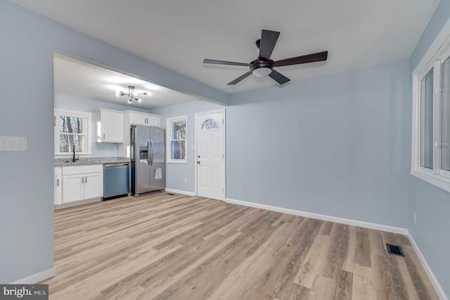 kitchen featuring white cabinetry, sink, stainless steel appliances, light hardwood / wood-style floors, and ceiling fan with notable chandelier