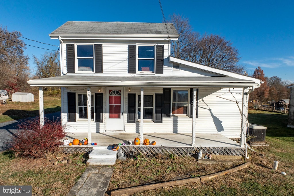 view of front of property with a front yard, a porch, central AC, and a storage shed