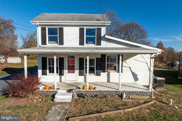 view of front of property with a front yard, a porch, central AC, and a storage shed