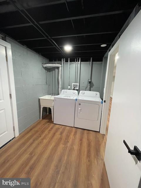 clothes washing area with hardwood / wood-style floors, washing machine and dryer, and sink