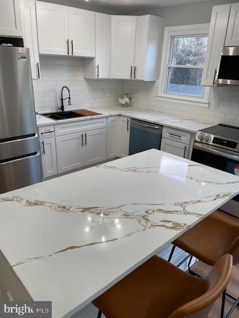 kitchen featuring light stone countertops, sink, a breakfast bar area, white cabinets, and appliances with stainless steel finishes