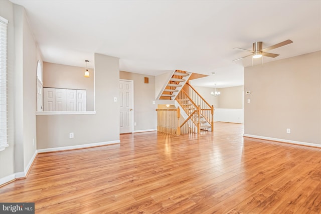 unfurnished living room with ceiling fan with notable chandelier and light wood-type flooring