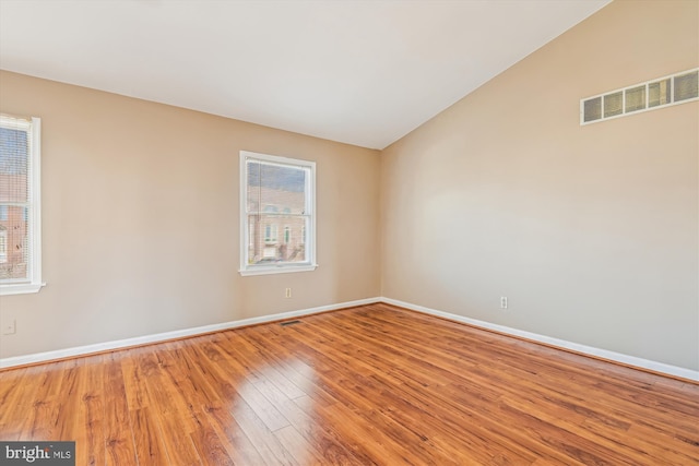 empty room featuring vaulted ceiling, a healthy amount of sunlight, and hardwood / wood-style floors