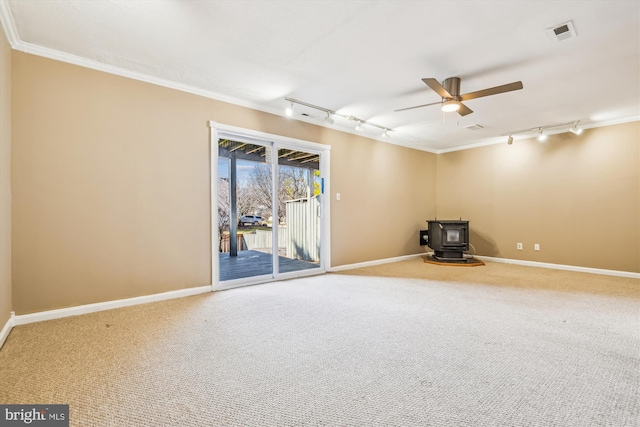 spare room with ceiling fan, ornamental molding, carpet, and a wood stove