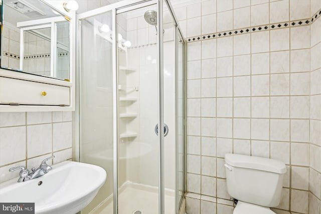 bathroom with toilet, a shower with shower door, sink, tasteful backsplash, and tile walls