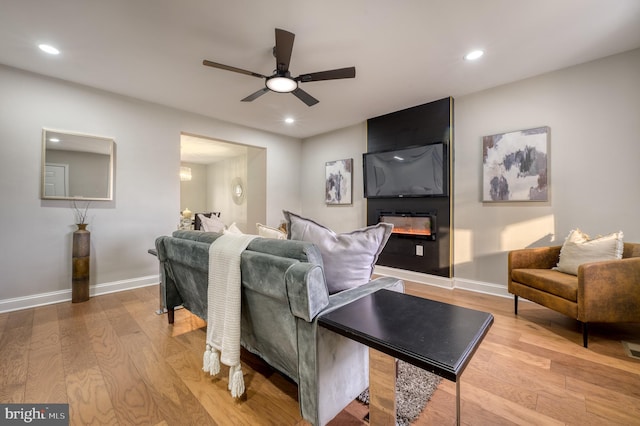 living room with ceiling fan, a large fireplace, and light hardwood / wood-style flooring