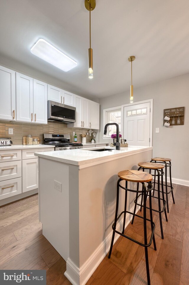 kitchen with pendant lighting, light hardwood / wood-style floors, white cabinetry, and stainless steel appliances