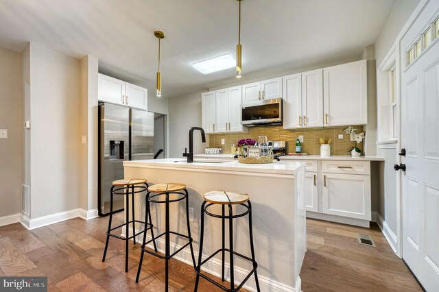 kitchen with stainless steel appliances, sink, hardwood / wood-style flooring, white cabinets, and hanging light fixtures