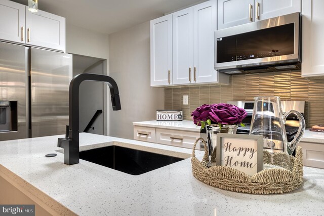 kitchen with light stone countertops, stainless steel appliances, white cabinetry, and tasteful backsplash