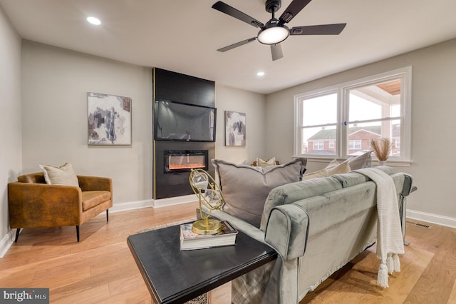 living room with ceiling fan, a fireplace, and light hardwood / wood-style floors