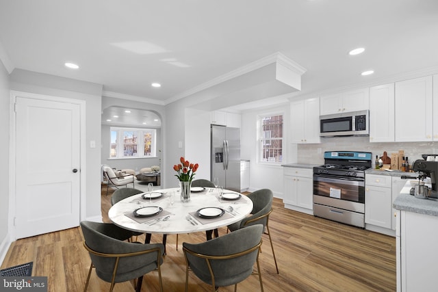 kitchen featuring white cabinets, appliances with stainless steel finishes, light hardwood / wood-style flooring, and crown molding