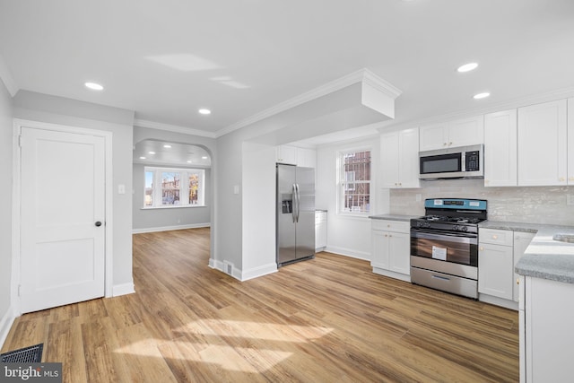 kitchen with crown molding, light hardwood / wood-style flooring, appliances with stainless steel finishes, tasteful backsplash, and white cabinetry