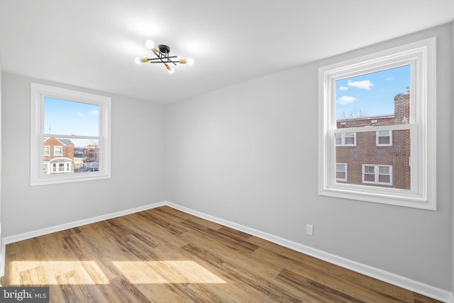 unfurnished room featuring a chandelier, hardwood / wood-style floors, and a healthy amount of sunlight