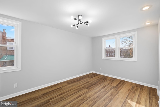 empty room with a healthy amount of sunlight, wood-type flooring, and an inviting chandelier